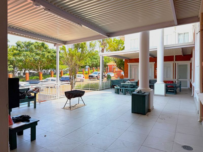 A spacious covered outdoor patio area featuring tiled flooring, structural columns, and a corrugated metal roof, suitable for office break times or outdoor meetings.