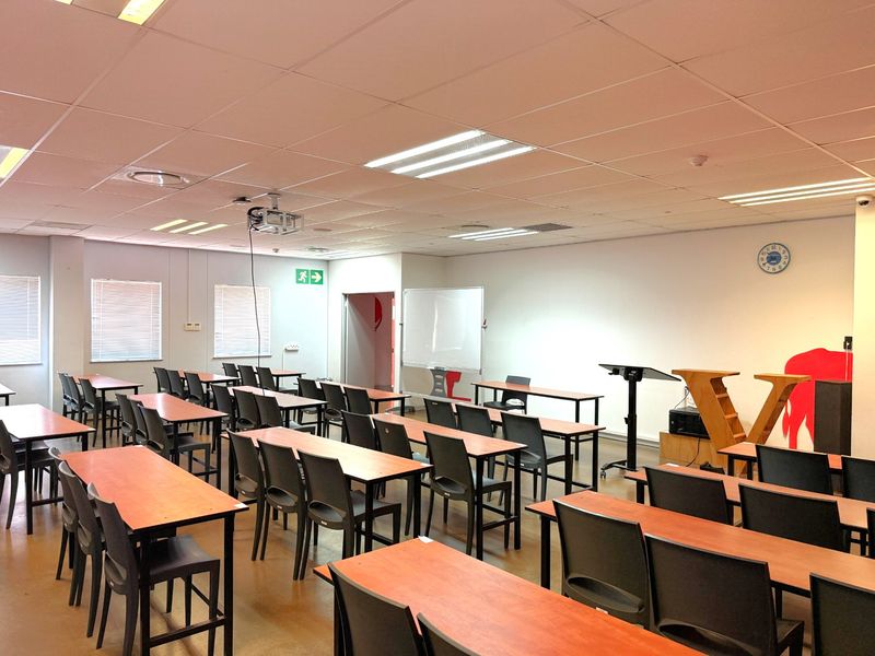 A functional office training room featuring a suspended ceiling, recessed lighting, projector, and multiple rows of desks arranged for classroom-style seating.