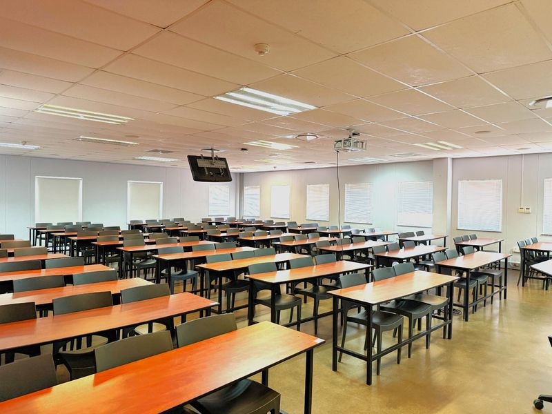 A spacious office or training room featuring a suspended ceiling, recessed lighting, and multiple windows with fitted blinds.