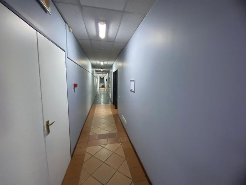 A long industrial hallway featuring tiled flooring, a suspended ceiling with integrated lighting, and multiple access doors.
