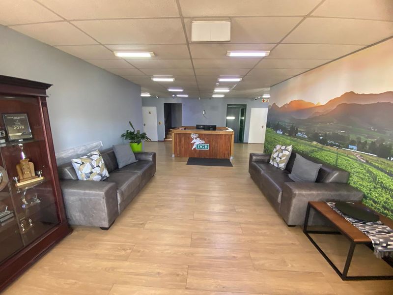 A professional industrial reception area featuring a built-in reception desk, laminate flooring, and a suspended ceiling with recessed lighting.