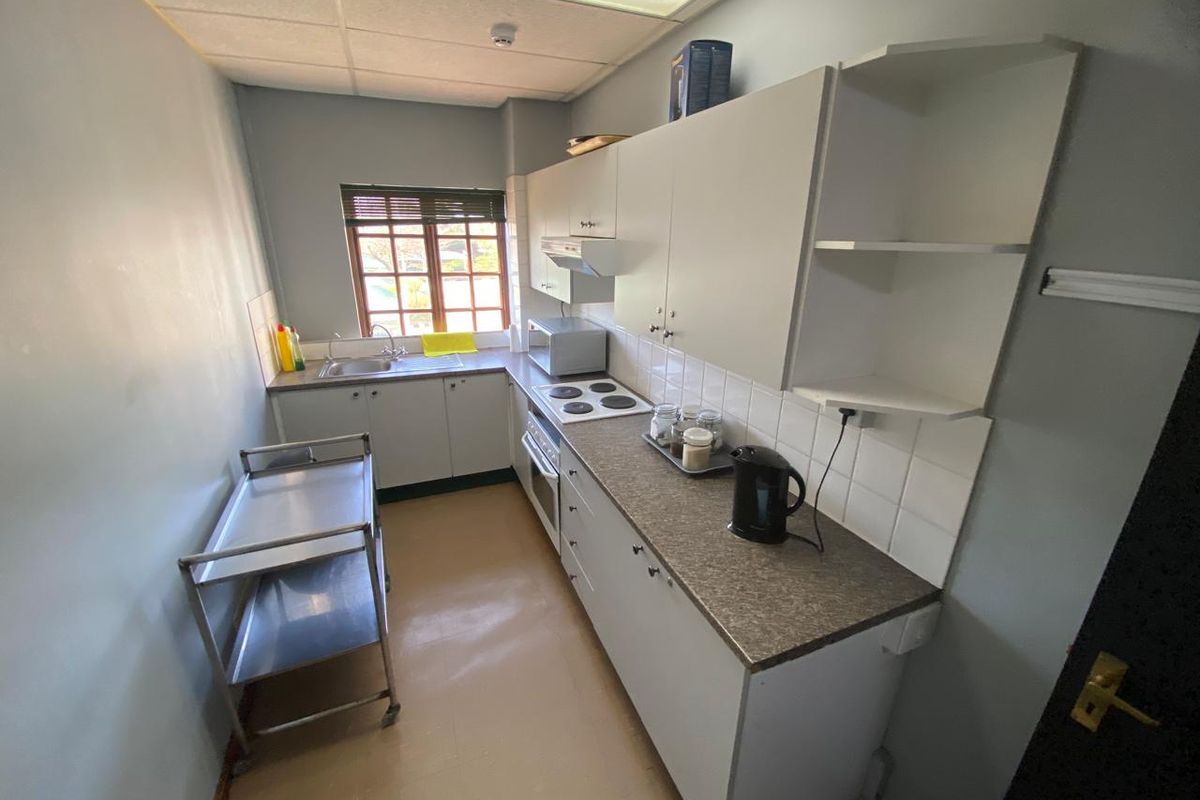 A functional galley-style kitchen featuring built-in cabinetry, laminate countertops, an electric hob, and a stainless steel sink with tiled splashback.