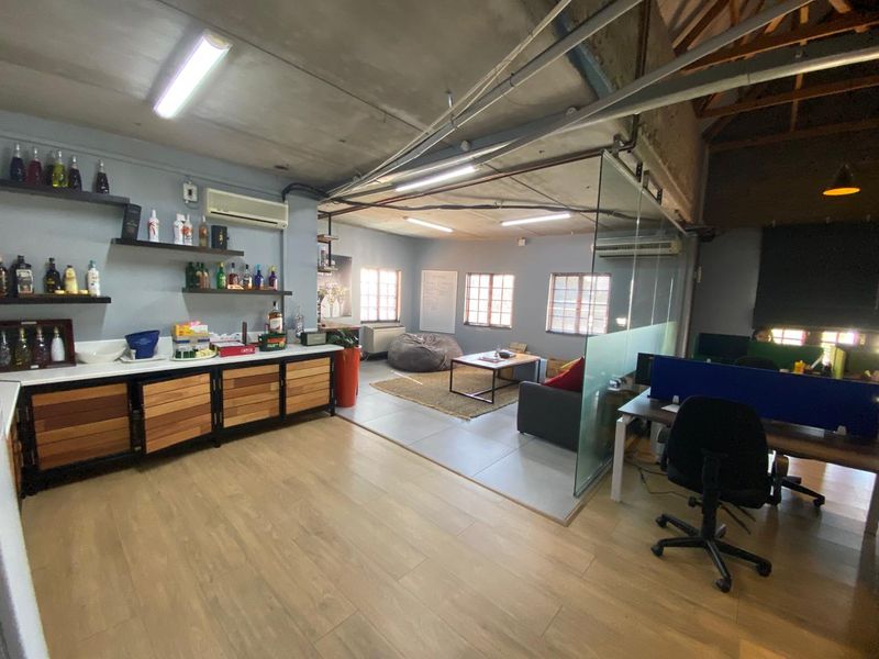 An open-plan industrial office space featuring exposed concrete ceilings, glass partitioning, built-in cabinetry, and a mix of laminate and tiled flooring.