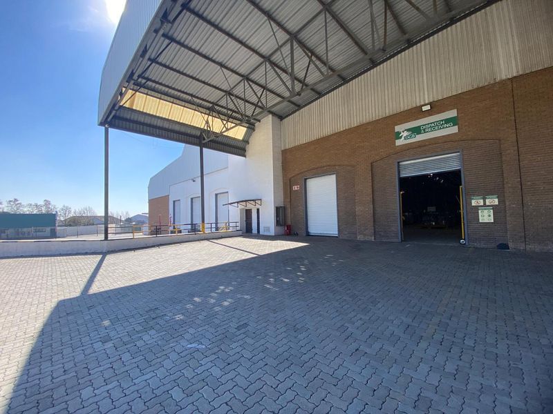 Industrial loading and dispatch area featuring a paved yard, large roller shutter doors, and a high-clearance steel canopy structure.