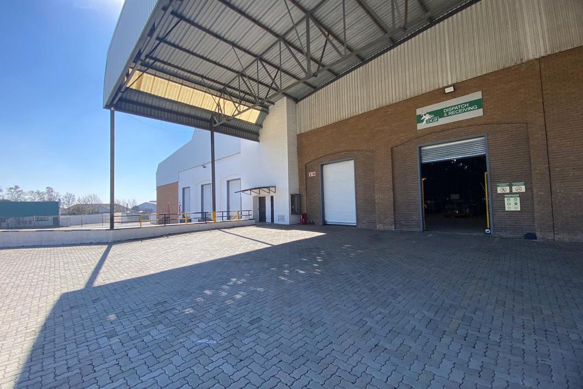 Industrial loading and dispatch area featuring a paved yard, large roller shutter doors, and a high-clearance steel canopy structure.