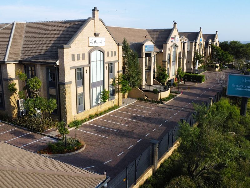 Aerial view of a multi-unit office complex featuring brick facades, tiled roofing, and an extensive paved parking area with perimeter security fencing.