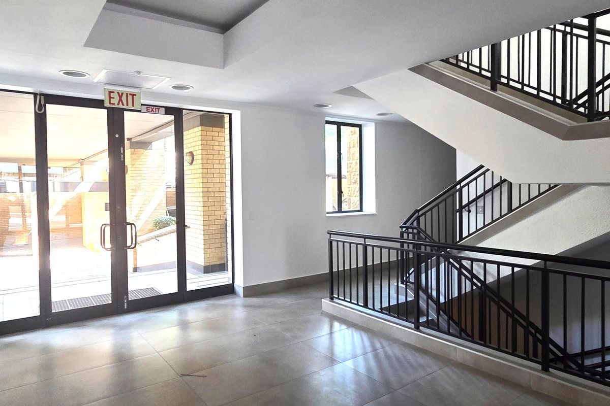 A bright and modern office building entrance lobby featuring tiled flooring, a prominent staircase with metal balustrades, and large glass doors.