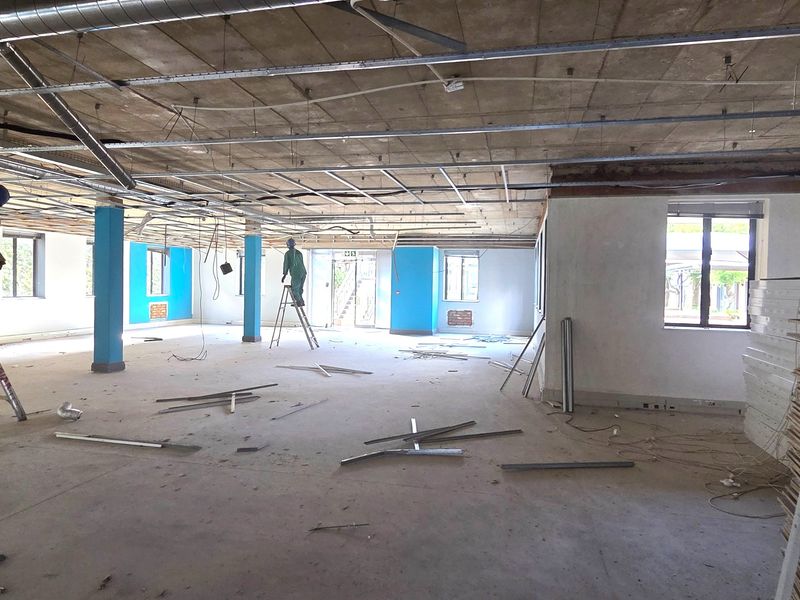 Open-plan office space currently undergoing renovation, featuring exposed concrete ceilings, structural columns, and large windows providing natural light.