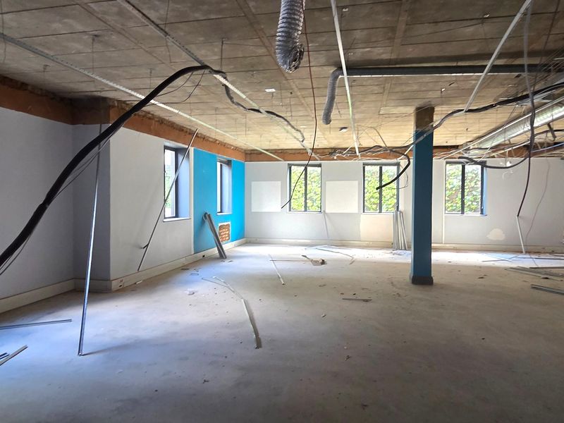 An open-plan office space currently undergoing renovation, featuring exposed concrete ceilings, ductwork, and large windows, providing a blank canvas for custom fit-out.