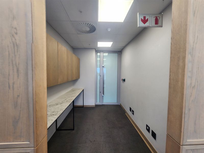A clean, modern office hallway featuring built-in cabinetry, a stone-topped console, carpeted flooring, and a frosted glass door leading to an adjacent space.