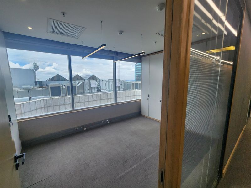 A bright, empty office space featuring large windows, built-in storage cabinetry, modern suspended lighting, and a glass partition wall.