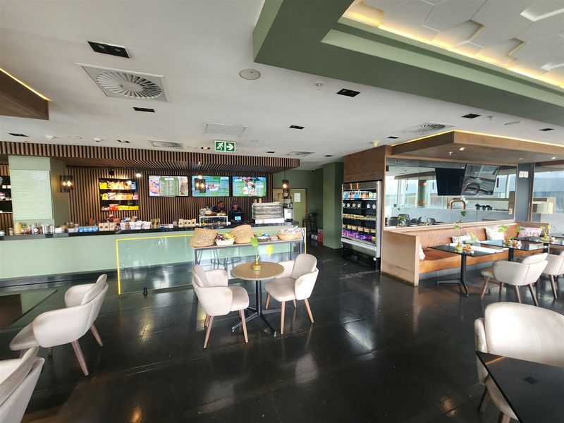 A modern, well-maintained open-plan office cafe area featuring a service counter, built-in booth seating, and sophisticated coffered ceiling lighting.