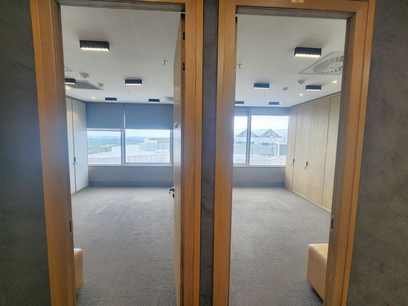 Two adjacent empty office spaces featuring neutral carpeting, built-in storage cabinetry, recessed ceiling lighting, and large windows providing natural light and exterior views.