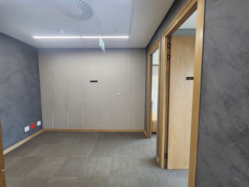 A vacant office space featuring acoustic wall paneling, carpet tiles, and a suspended ceiling with recessed lighting.