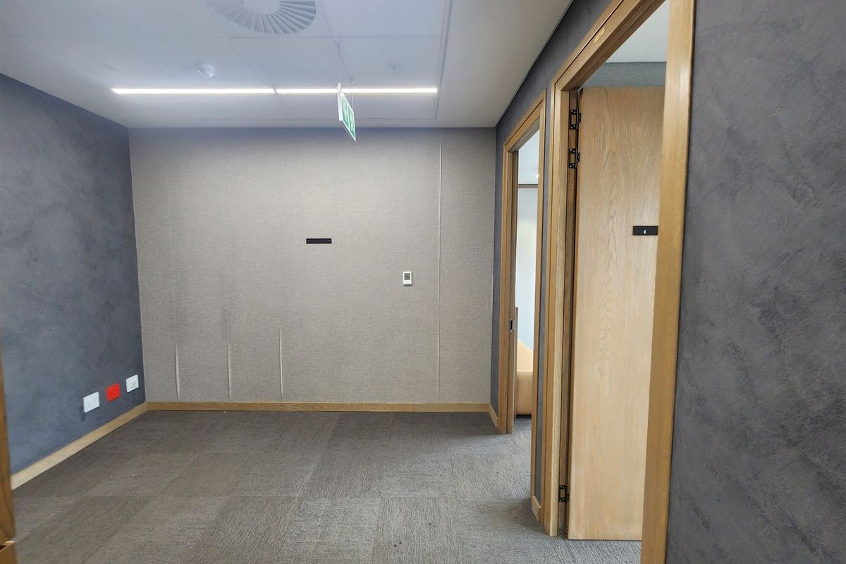 A vacant office space featuring acoustic wall paneling, carpet tiles, and a suspended ceiling with recessed lighting.