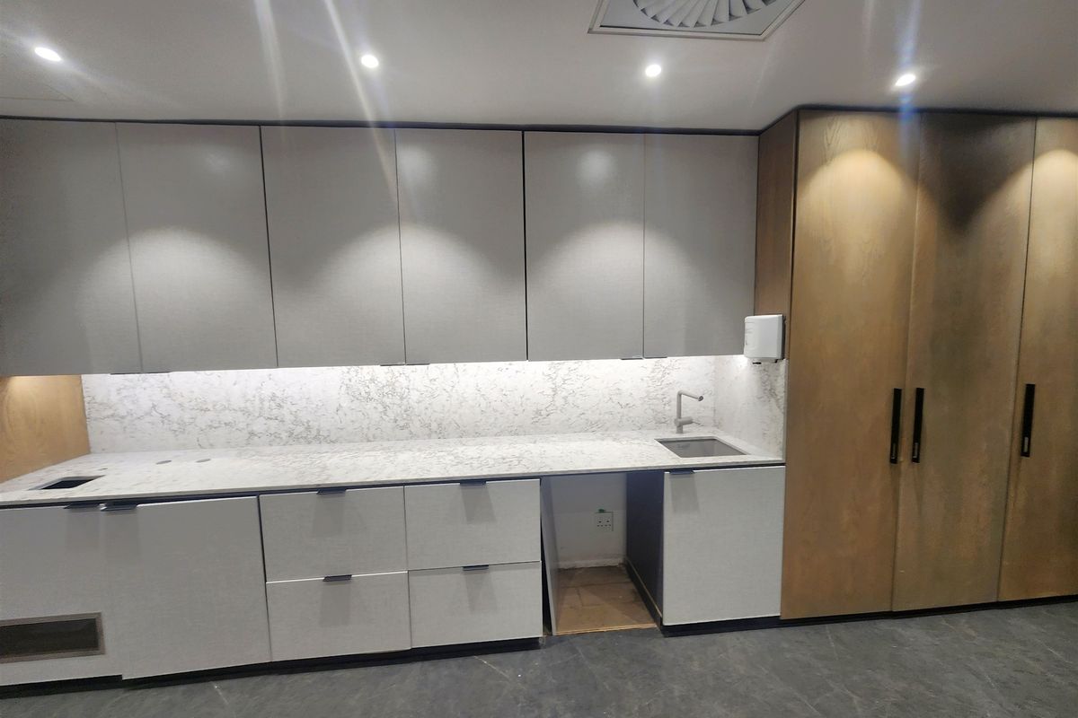 Modern office kitchenette featuring sleek grey and wood-tone cabinetry, stone countertops, integrated sink, and recessed lighting, providing a clean and functional workspace.