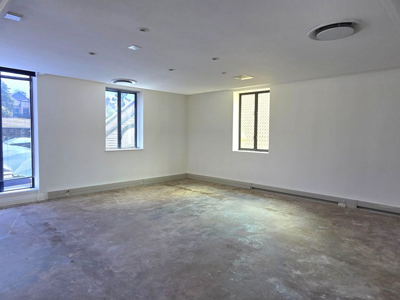 A spacious, empty office area featuring white walls, recessed ceiling lighting, ducted air conditioning, and unfinished concrete flooring ready for new floor finishes.