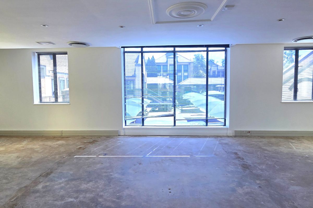 Spacious, empty office area featuring large windows with blinds, recessed ceiling lighting, and unfinished concrete flooring, ready for custom fit-out.