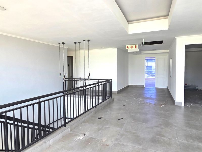 Spacious office hallway featuring tiled flooring, a metal balustrade overlooking the lower level, and modern pendant lighting.