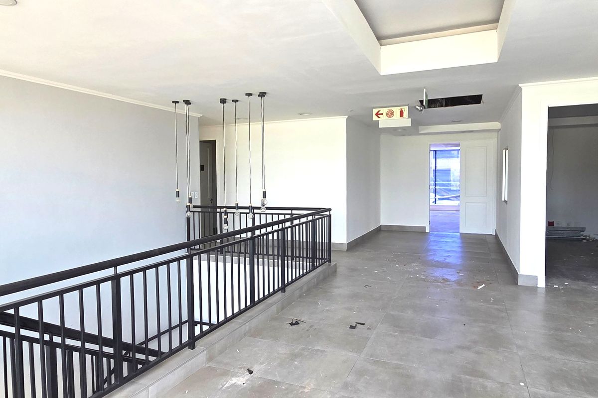 Spacious office hallway featuring tiled flooring, a metal balustrade overlooking the lower level, and modern pendant lighting.