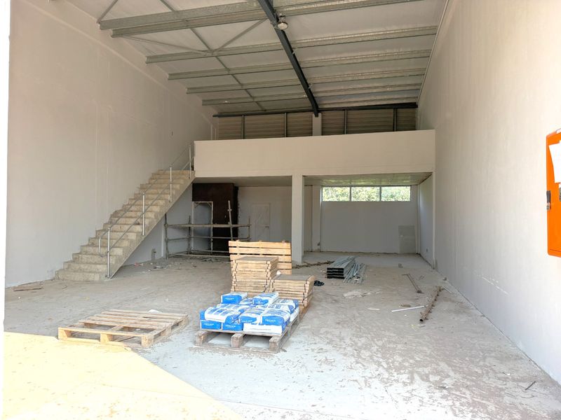 Spacious industrial warehouse unit featuring a mezzanine level, concrete staircase, and high ceilings, currently in an unfinished shell condition suitable for various commercial uses.