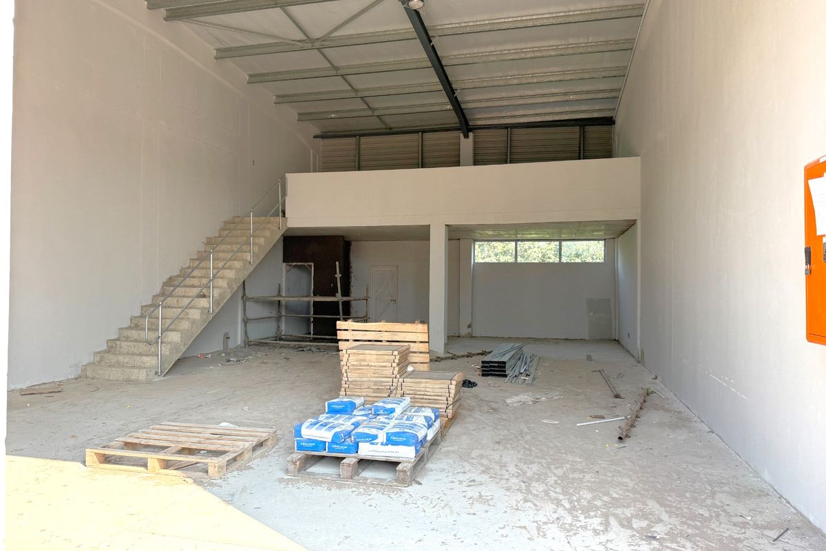 Spacious industrial warehouse unit featuring a mezzanine level, concrete staircase, and high ceilings, currently in an unfinished shell condition suitable for various commercial uses.