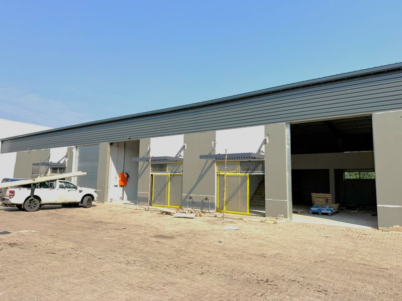 Industrial warehouse facility featuring multiple roller shutter doors, metal roof cladding, and a large concrete paved yard area currently under final construction stages.