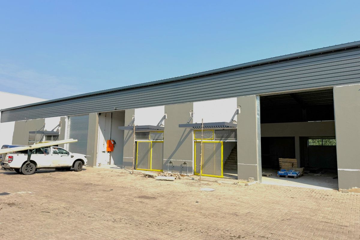 Industrial warehouse facility featuring multiple roller shutter doors, metal roof cladding, and a large concrete paved yard area currently under final construction stages.
