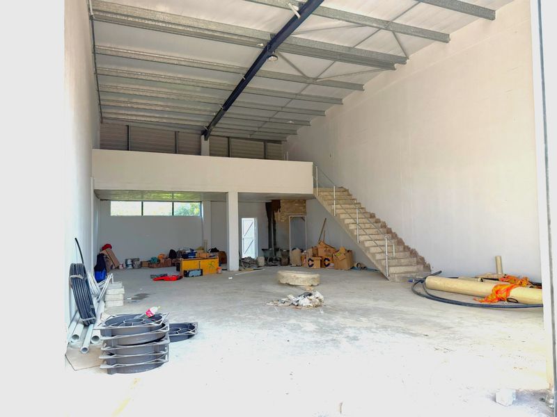 Spacious industrial warehouse unit featuring a mezzanine level, concrete staircase, and high ceilings with exposed steel structural elements.