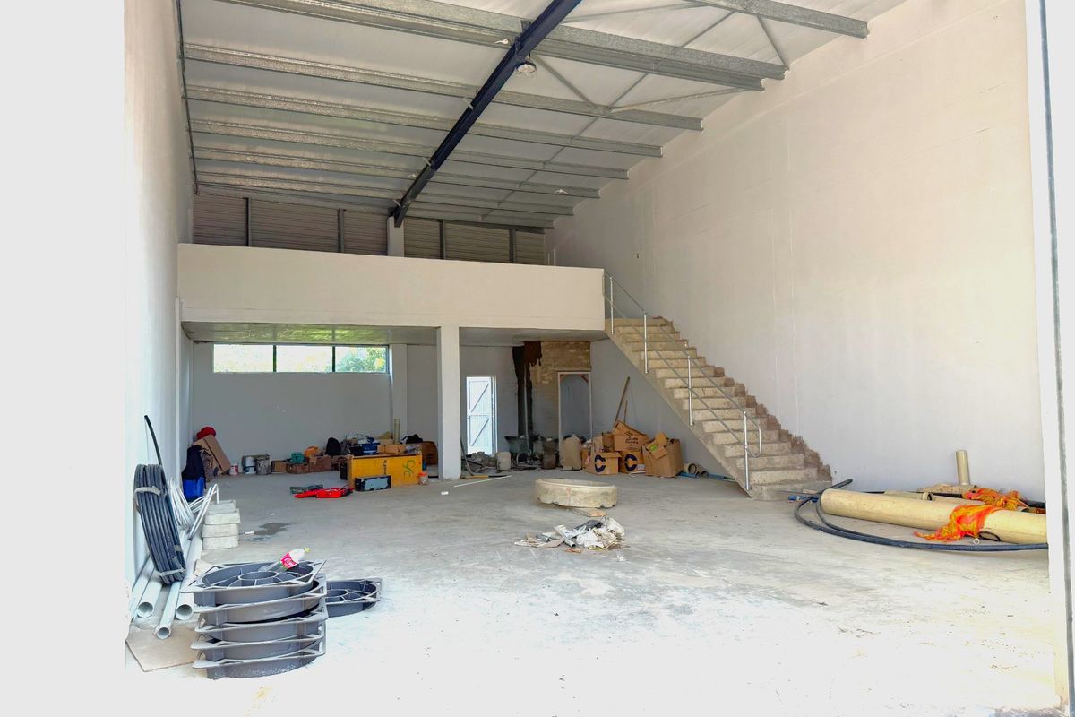 Spacious industrial warehouse unit featuring a mezzanine level, concrete staircase, and high ceilings with exposed steel structural elements.