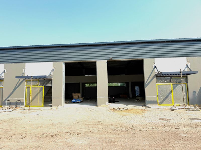 Front elevation of an industrial warehouse unit featuring metal cladding, concrete pillars, and large sliding glass doors with modern awning structures.
