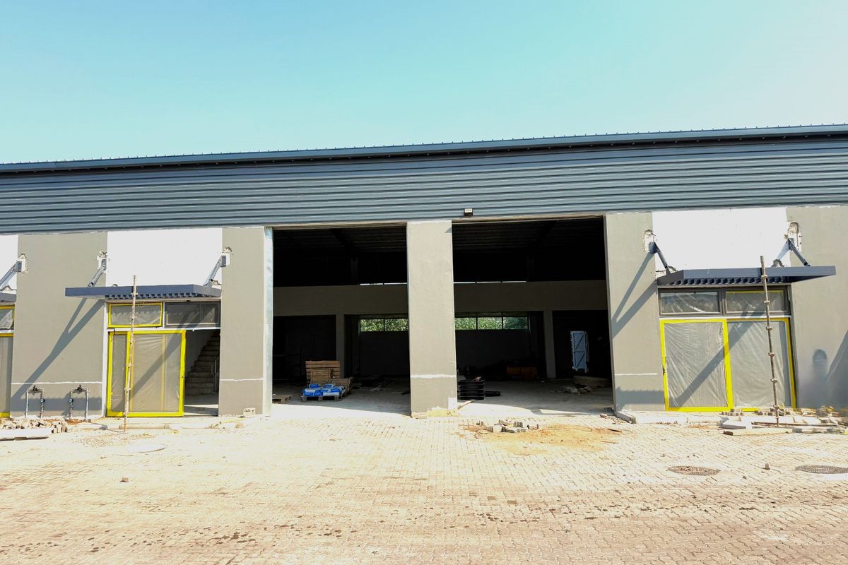 Front elevation of an industrial warehouse unit featuring metal cladding, concrete pillars, and large sliding glass doors with modern awning structures.