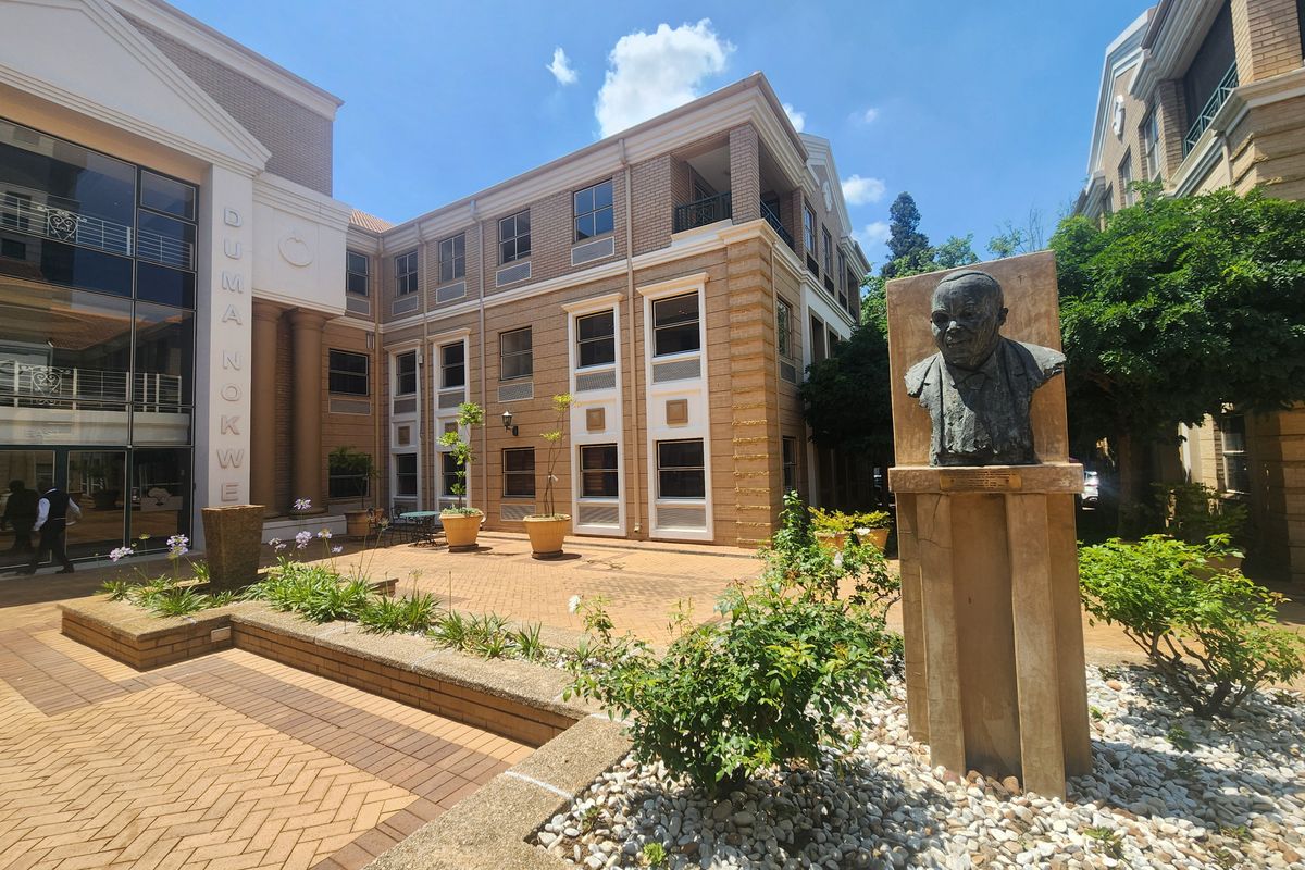A well-maintained office building exterior featuring a paved courtyard, landscaped garden areas, and a prominent bronze monument.