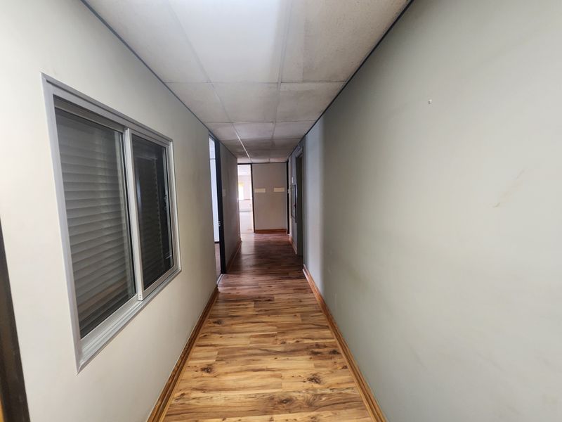 A vacant office hallway featuring wood-look laminate flooring, a suspended ceiling, and neutral wall finishes.