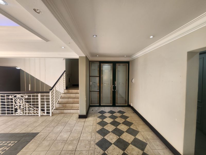 Spacious office entrance foyer featuring decorative crown molding, recessed lighting, a tiled floor with a diamond pattern inlay, and a wrought iron staircase.