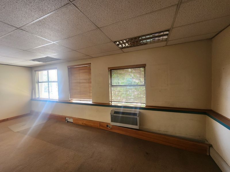 An empty office space featuring a suspended ceiling, recessed lighting, wall-mounted air conditioning, and timber dado rail detailing.