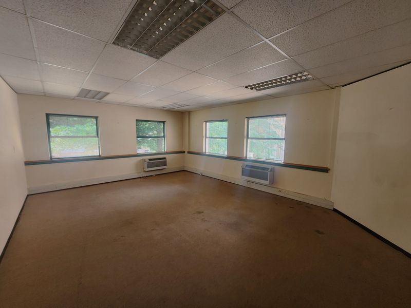 An empty office space featuring a suspended ceiling with recessed lighting, wall-mounted air conditioning units, and carpeted flooring.