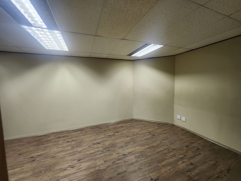 A clean, empty office space featuring modern laminate flooring, a suspended ceiling with recessed lighting, and neutral wall finishes.