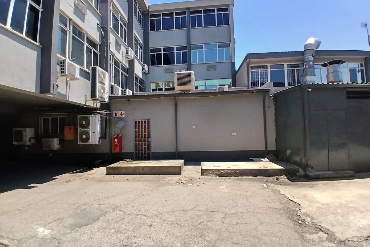 Rear exterior view of the office building featuring asphalt paving, multiple wall-mounted air conditioning units, and industrial ventilation ducting.