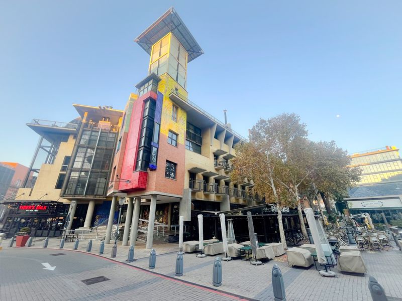 A vibrant multi-story commercial building featuring a distinctive architectural tower, external balconies, and a paved ground-level plaza area.