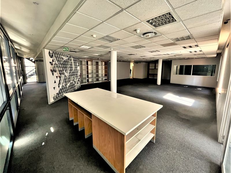 Spacious open-plan office area featuring a suspended ceiling, recessed lighting, built-in cabinetry, and large windows providing ample natural light.