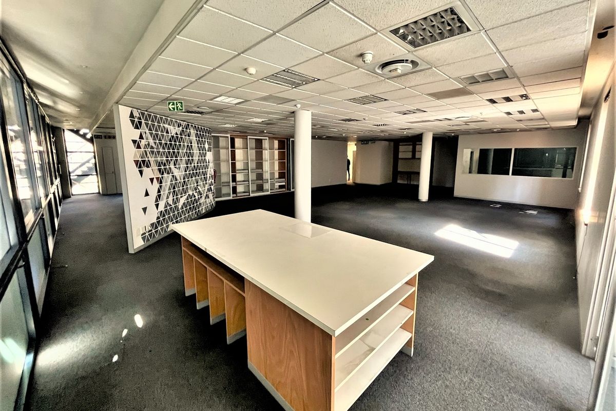 Spacious open-plan office area featuring a suspended ceiling, recessed lighting, built-in cabinetry, and large windows providing ample natural light.