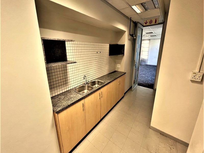 A compact office kitchenette featuring built-in cabinetry, a granite countertop with a double sink, and tiled backsplash, providing functional utility space.