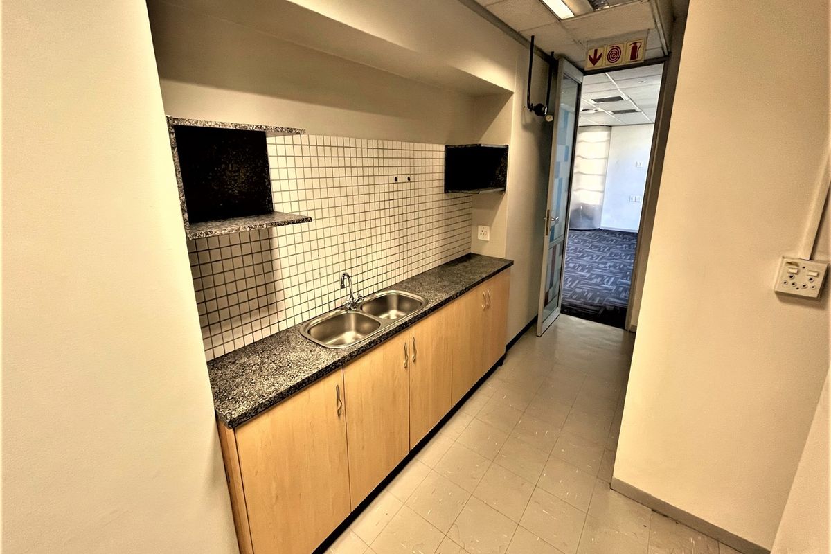 A compact office kitchenette featuring built-in cabinetry, a granite countertop with a double sink, and tiled backsplash, providing functional utility space.