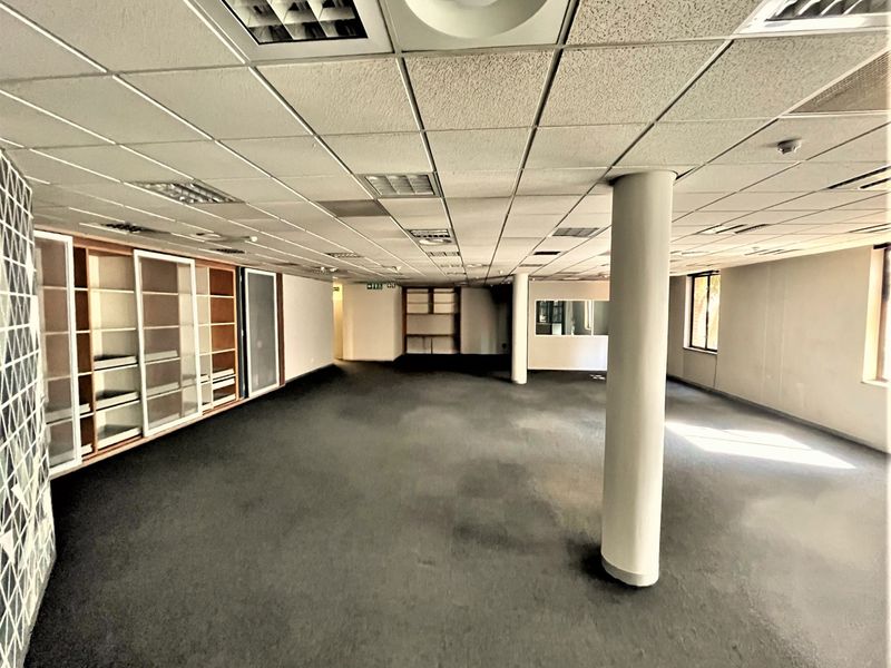 Spacious open-plan office area featuring a suspended ceiling, structural columns, and extensive built-in shelving units, offering a versatile workspace layout.