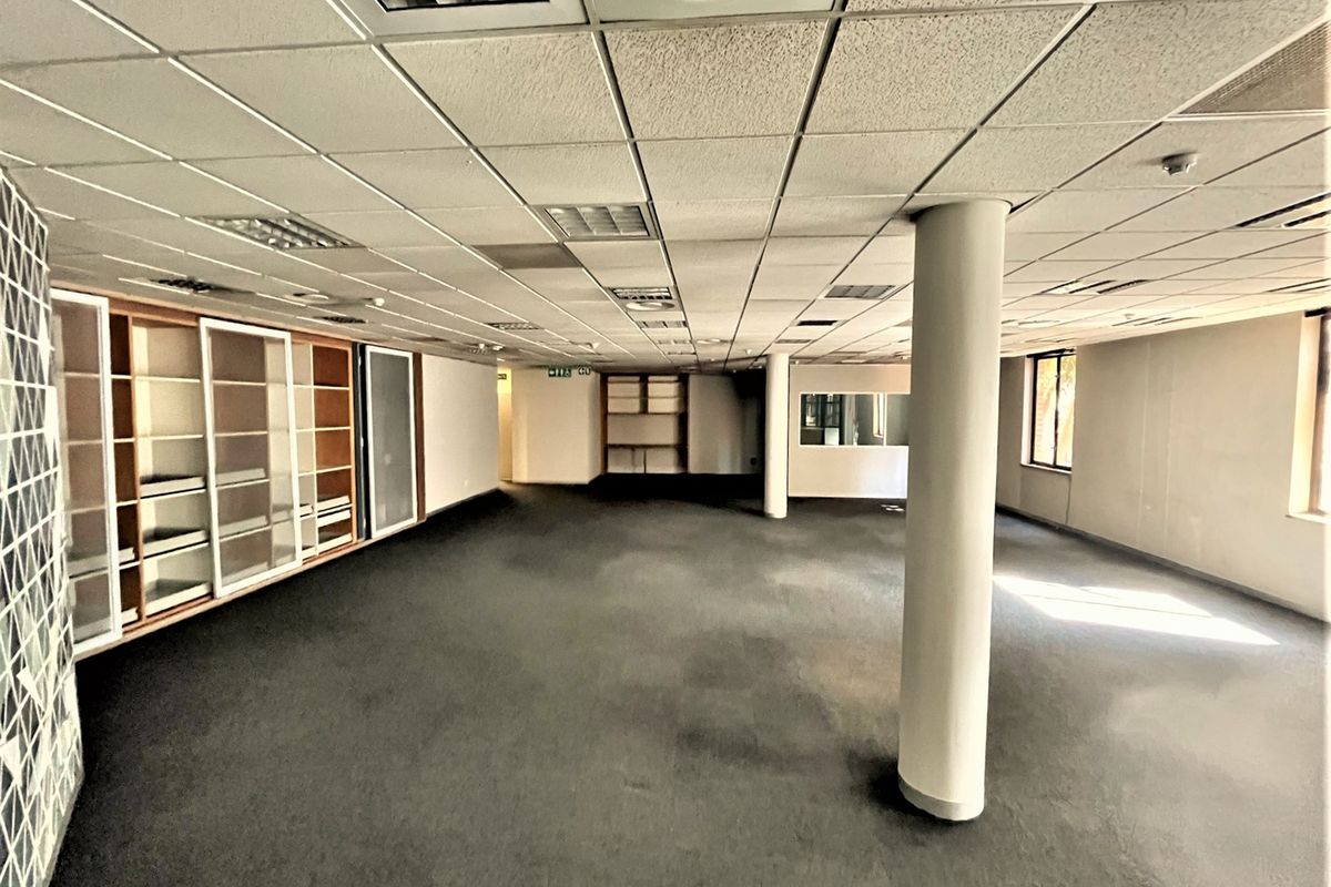 Spacious open-plan office area featuring a suspended ceiling, structural columns, and extensive built-in shelving units, offering a versatile workspace layout.