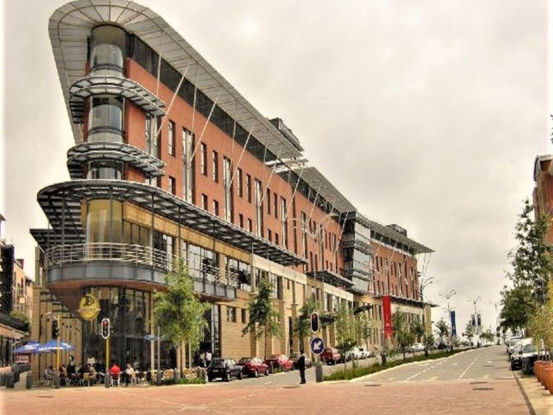 A modern multi-story office building featuring a distinctive curved glass facade, brick exterior, and integrated street-level commercial space with a paved plaza.