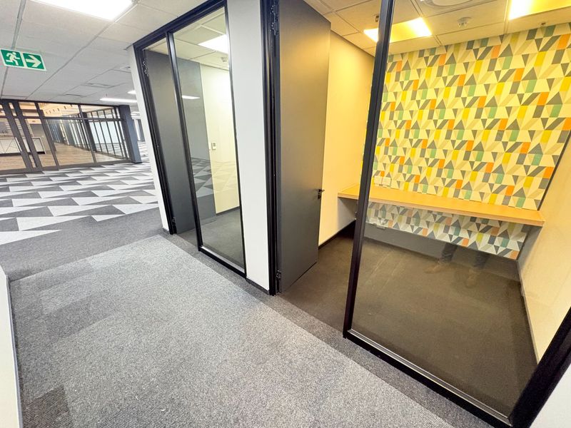 A modern office space featuring glass partitions, a built-in desk, patterned feature wall, and professional carpet tiles in a clean, open-plan environment.