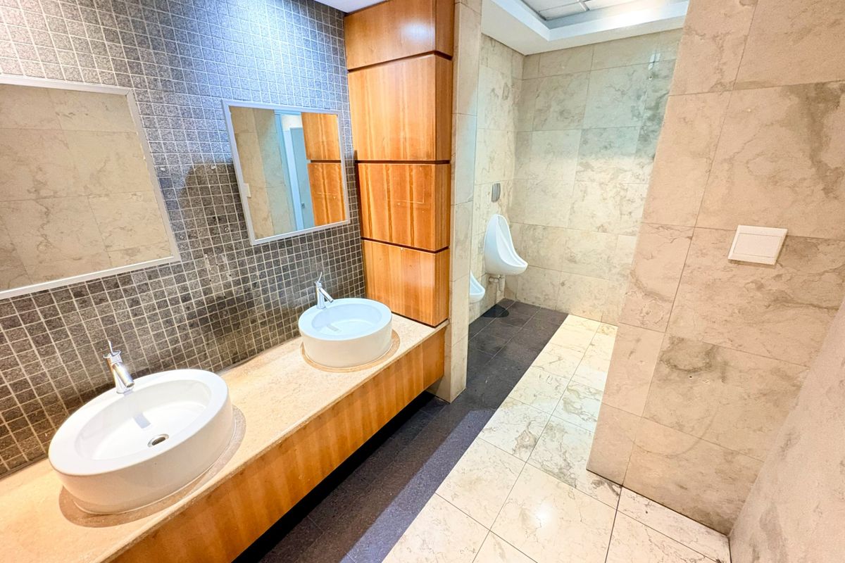 Modern office bathroom featuring a dual vessel sink vanity with stone countertop, wooden cabinetry, and tiled wall and floor finishes.