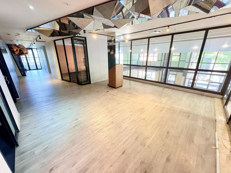 Spacious open-plan office area featuring modern laminate flooring, extensive glass partitioning, and a unique mirrored ceiling detail with integrated lighting.